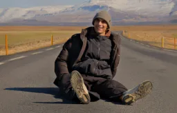 Keyan sits on an empty road, with snowy mountains behind him
