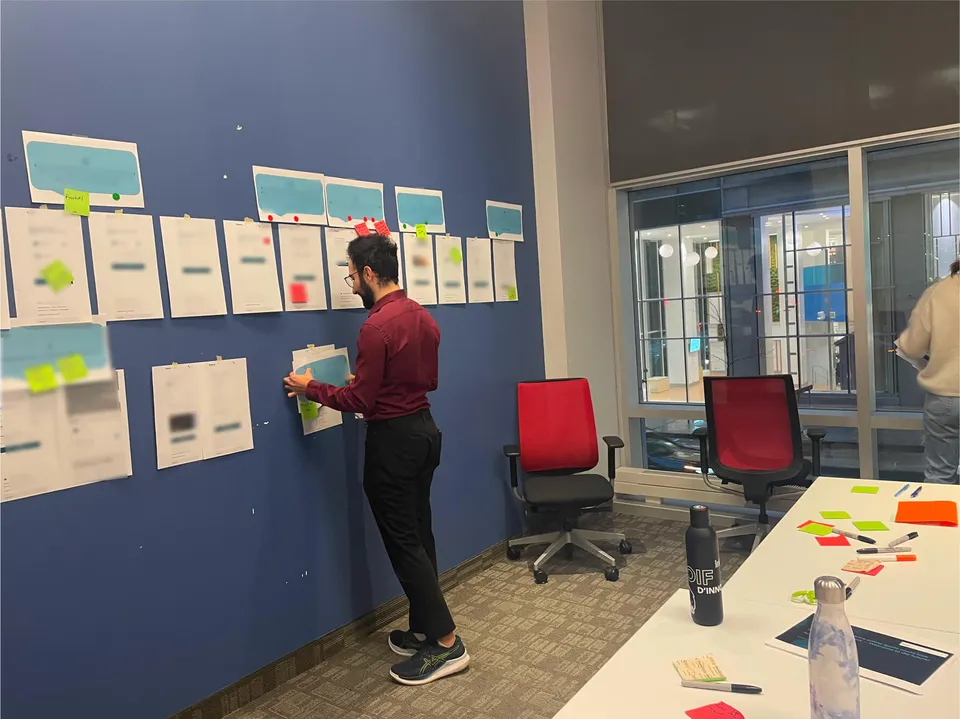 Keyan pins printed quote screens and sticky notes to a blue wall for the focus group, by a table of sticky notes