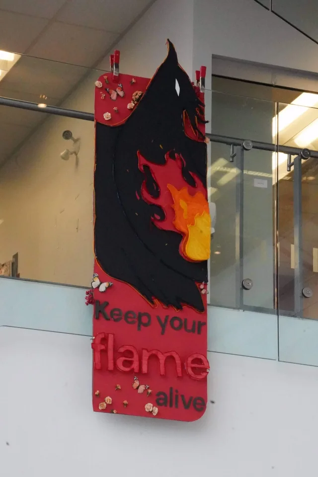 A red banner hung from a railing over a glass-walled hall, a black and orange flame over the words keep your flame alive
